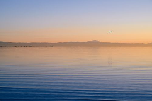 Free A serene view of an airplane flying over calm ocean waters during dawn, with mountains in the background. Stock Photo