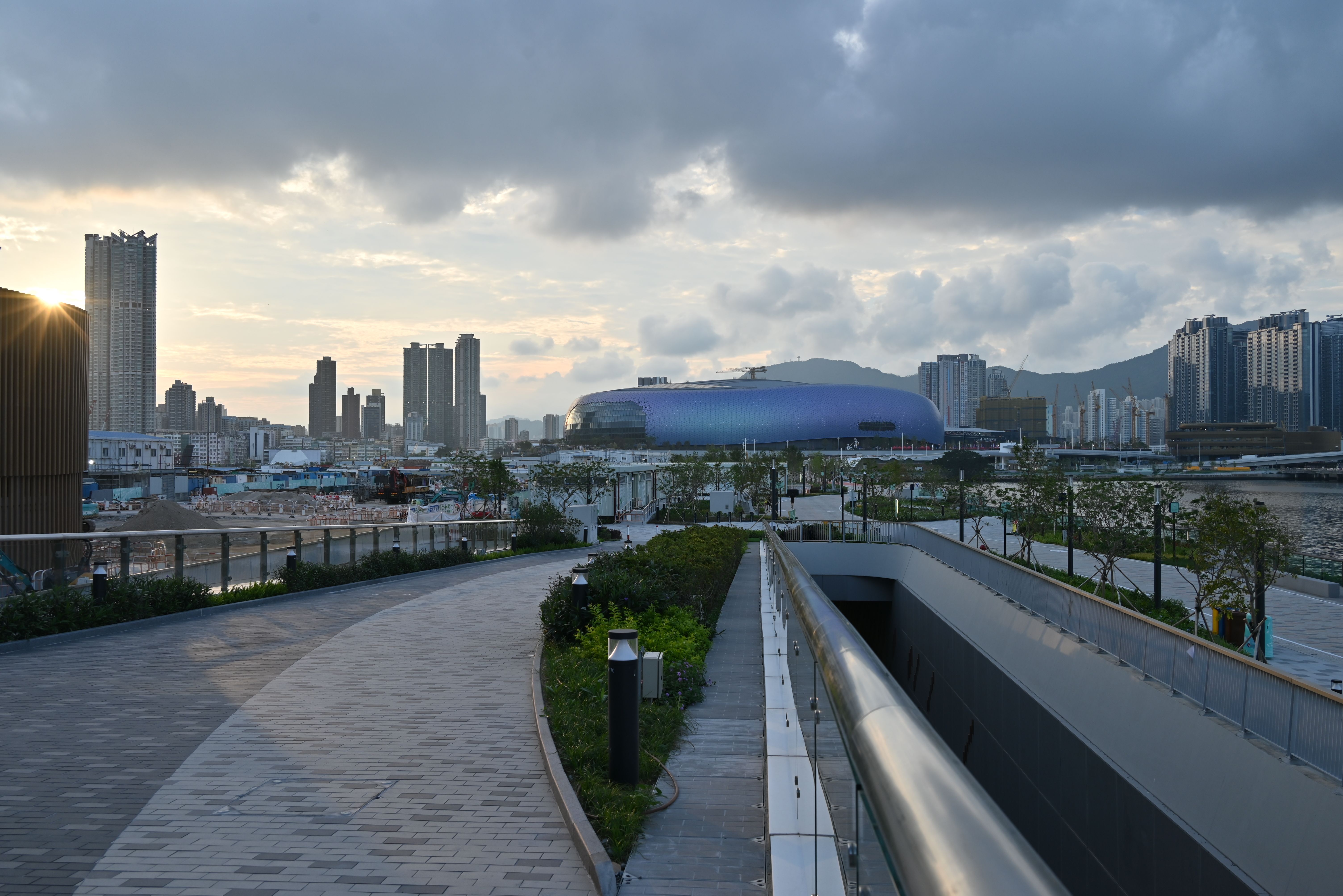 A Hong Kong racecourse at sunset, horses entering the starting gate, spectators studying race cards