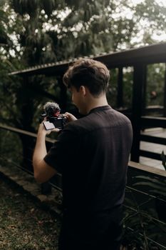 Back view of a young videographer capturing footage in a lush, outdoor setting.