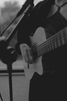 A person playing acoustic guitar in an atmospheric black and white setting.