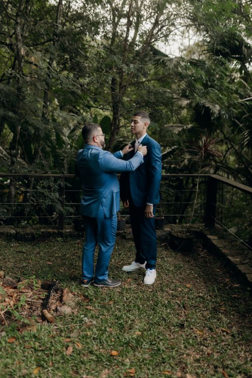 Free Two men preparing for a wedding, adjusting suits in a lush outdoor setting. Stock Photo