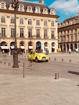 A vibrant yellow vintage car parked in a historical Paris square with classic architecture.