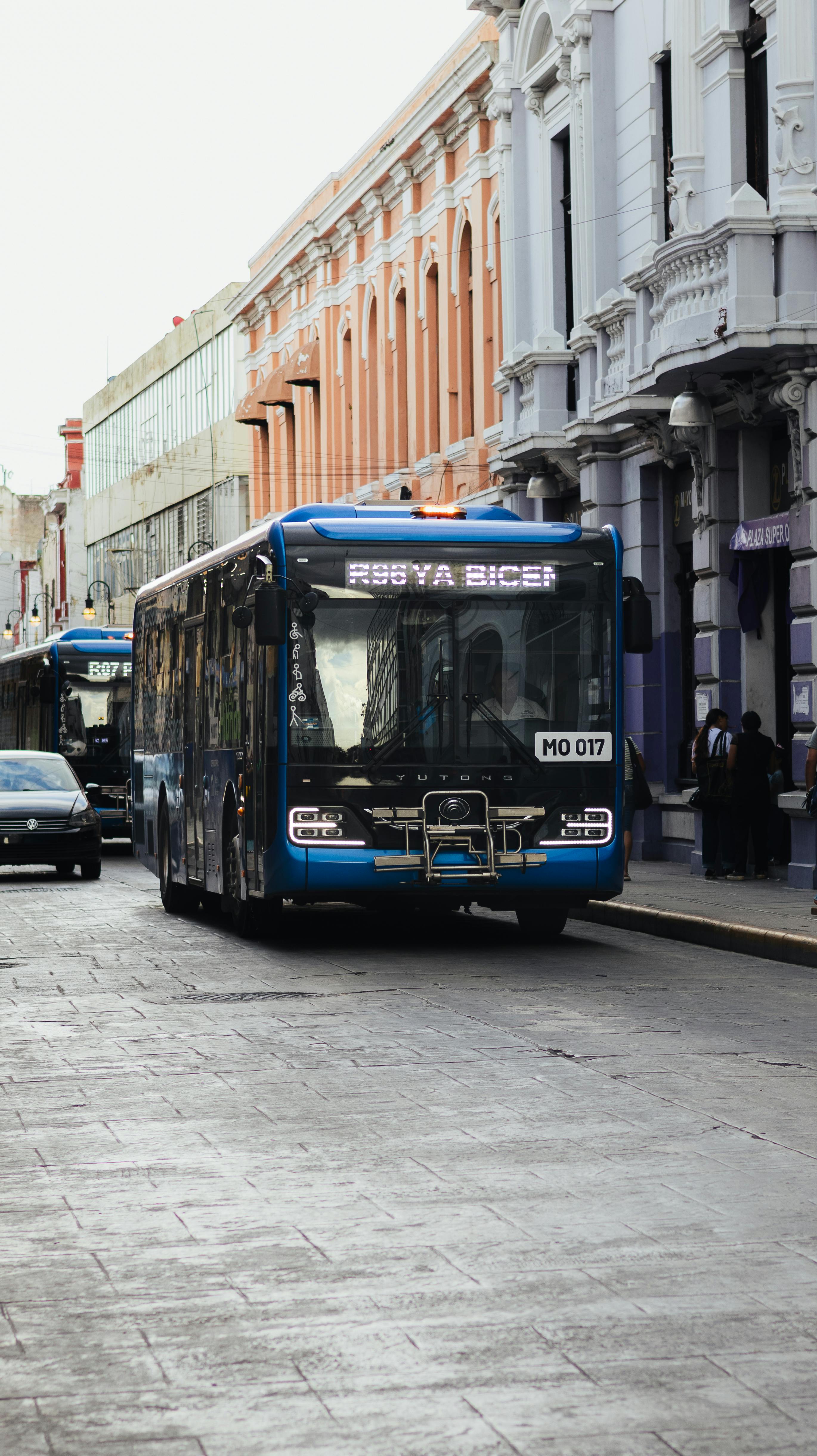 A blue bus travels down a historic street with classic European architecture buildings.