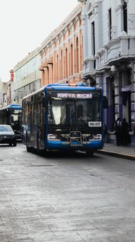 A blue bus travels down a historic street with classic European architecture buildings.