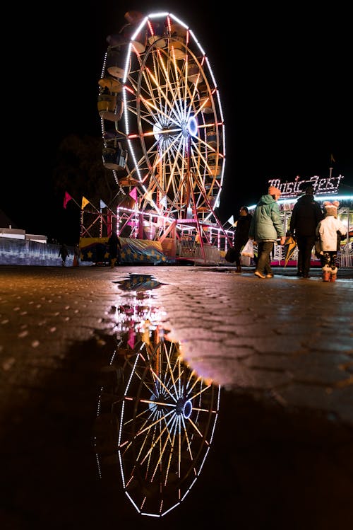 Lighted Ferris Wheel Reflection on Water Puddle at Night
