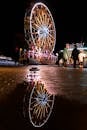 热闹的狂欢节上，充满活力的摩天轮夜景倒映在水坑中