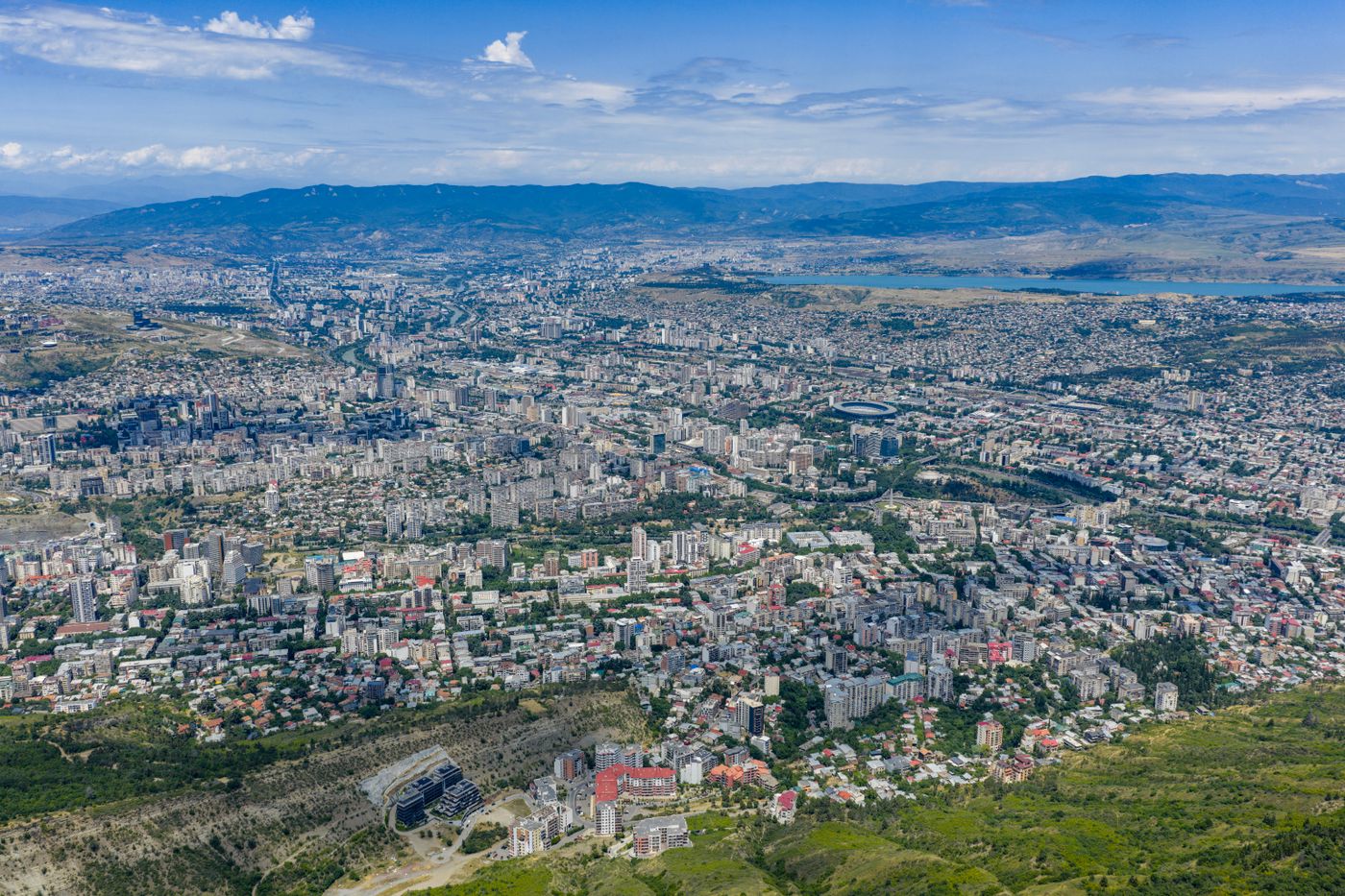 Aerial view of Tbilisi, Georgia (the Caucasus country), showing its sprawling urban cityscape against a backdrop of mountains.