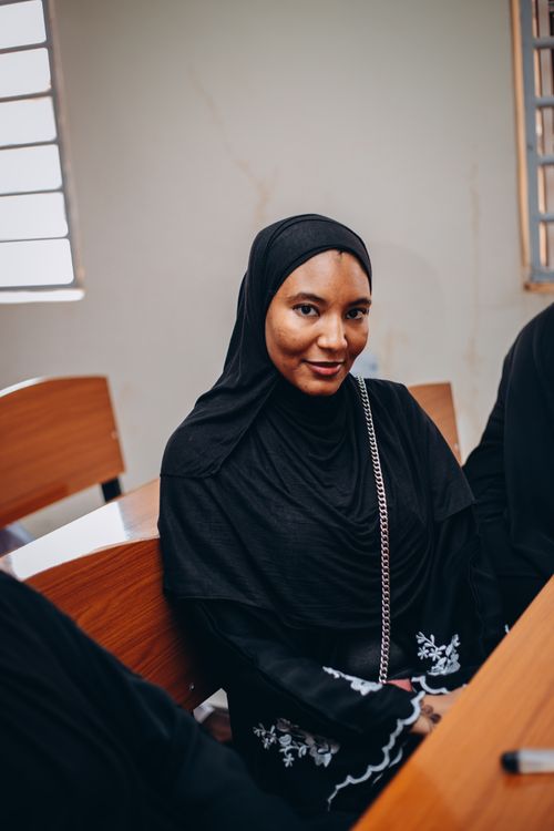 Free A smiling woman wearing a black abaya seated indoors with friends. Stock Photo