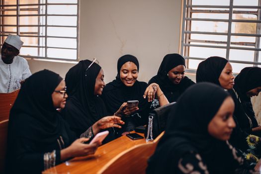 A group of women in hijabs sharing a joyful moment indoors, connected via smartphones.