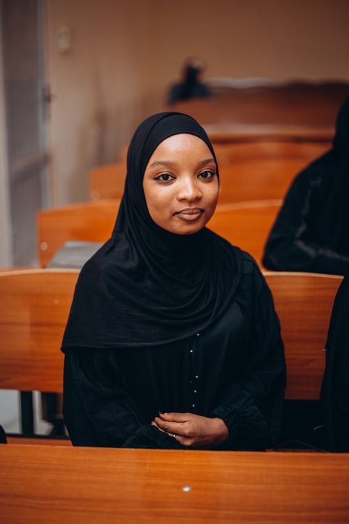 Free A young woman wearing a hijab sitting in a classroom, expressing a calm demeanor. Stock Photo