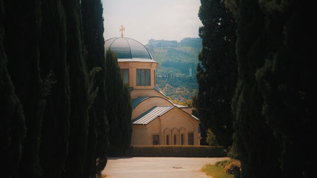 Serene chapel framed by tall cypress trees, set against rolling hills on a bright day.