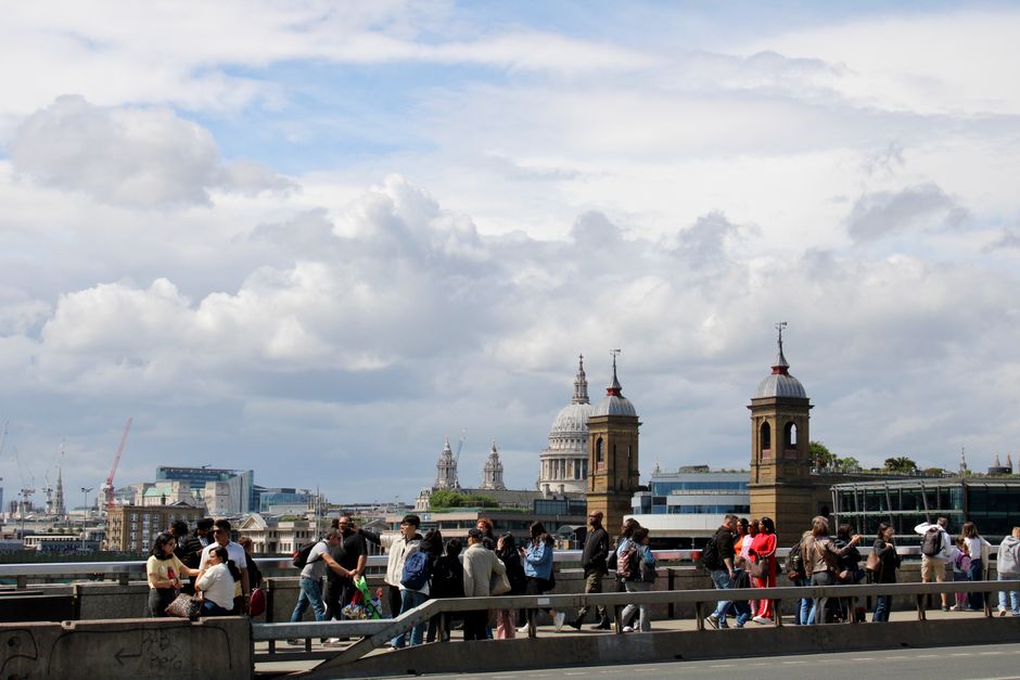 Crowds on London Bridge with cityscape including St. Paul's Cathedral under a cloudy sky.