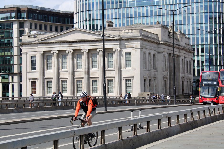Cyclist on London Bridge beside historic and modern architecture, sunny day.