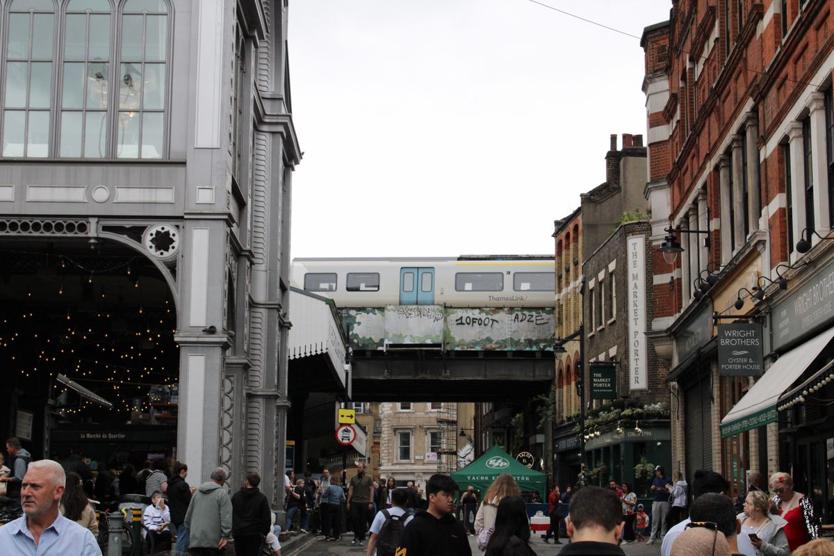 Scenă animată la Borough Market din Londra, cu trecători și un tren pe viaductul de deasupra
