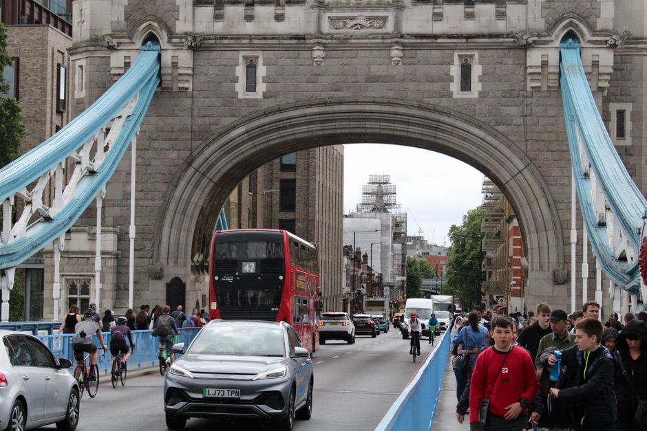 Crowds and traffic cross Tower Bridge in London, showcasing a busy urban scene.