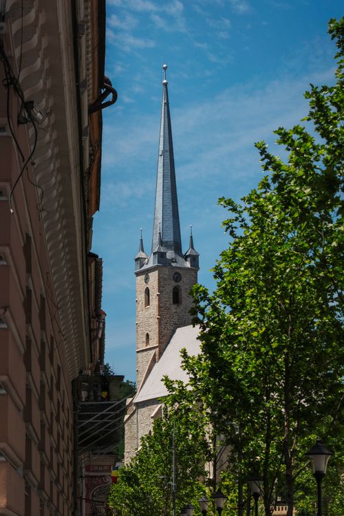 Free Gothic-style church tower surrounded by greenery and architectural buildings in Dej, Romania. Stock Photo
