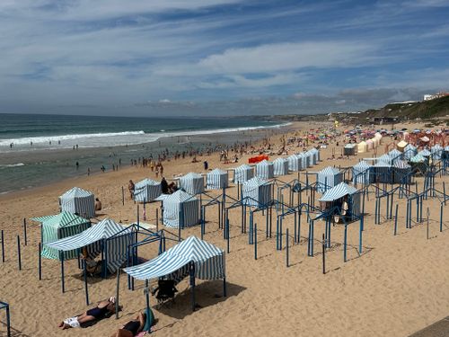 Free Sunny beach day at São Martinho do Porto with striped tents and crowds enjoying the summer. Stock Photo