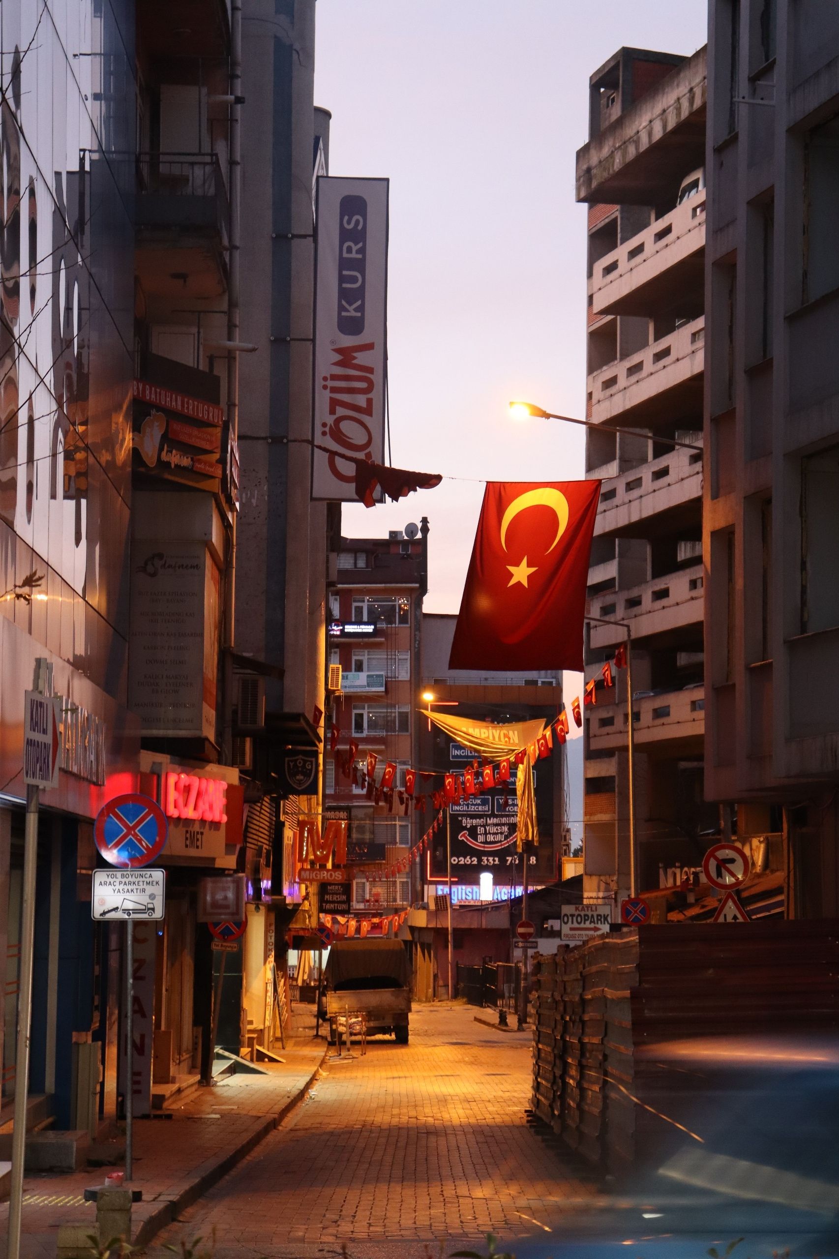 Charming street view in İzmit, Türkiye featuring Turkish flags at dusk, capturing urban life and architecture.