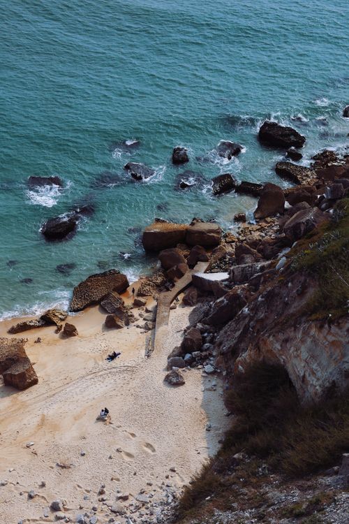 Free Stunning aerial shot of a rocky beach with turquoise waves crashing along the shore. Stock Photo