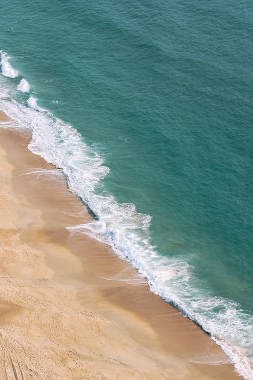 Free A serene beach with gentle waves lapping at golden sands, captured from above. Stock Photo
