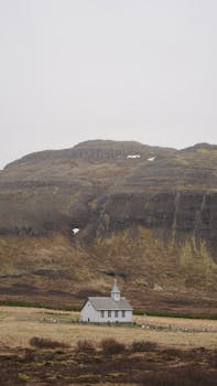 A solitary white church set against the rustic Icelandic hills, creating a serene and timeless scene.