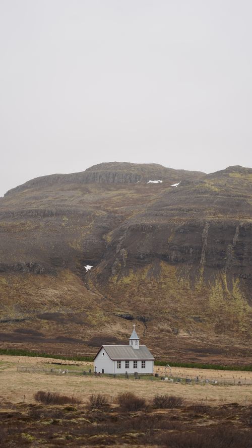 Free A solitary white church set against the rustic Icelandic hills, creating a serene and timeless scene. Stock Photo