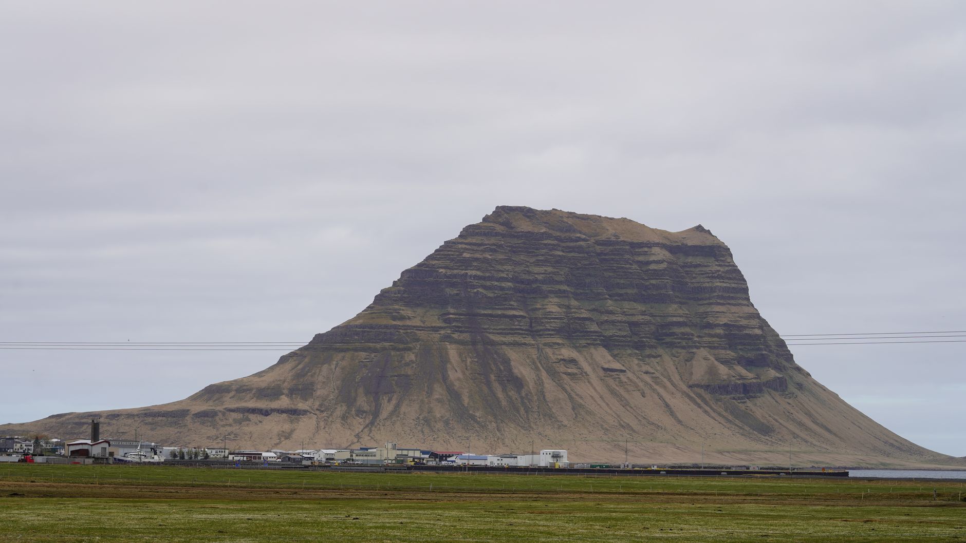 Stunning view of Kirkjufell Mountain under a cloudy sky in Iceland, highlighting its unique shape and the surrounding landscape.
