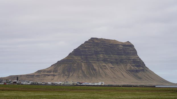 Stunning view of Kirkjufell Mountain under a cloudy sky in Iceland, highlighting its unique shape and the surrounding landscape.