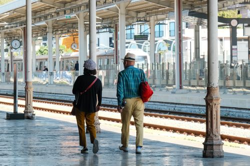 Free Elderly couple strolling in a sunlit train station, capturing a moment of leisure travel. Stock Photo