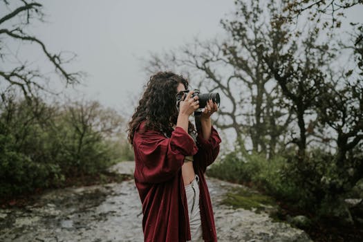 A young woman captures the misty forest landscape with her camera, embodying nature and exploration.