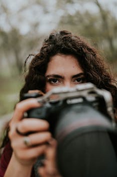 Close-up portrait of a photographer focusing on capturing a shot in a natural outdoor setting.