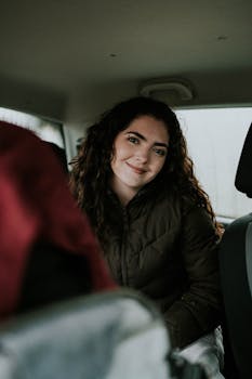 A young woman with curly hair smiles warmly inside a car, depicting a cozy and memorable road trip moment.