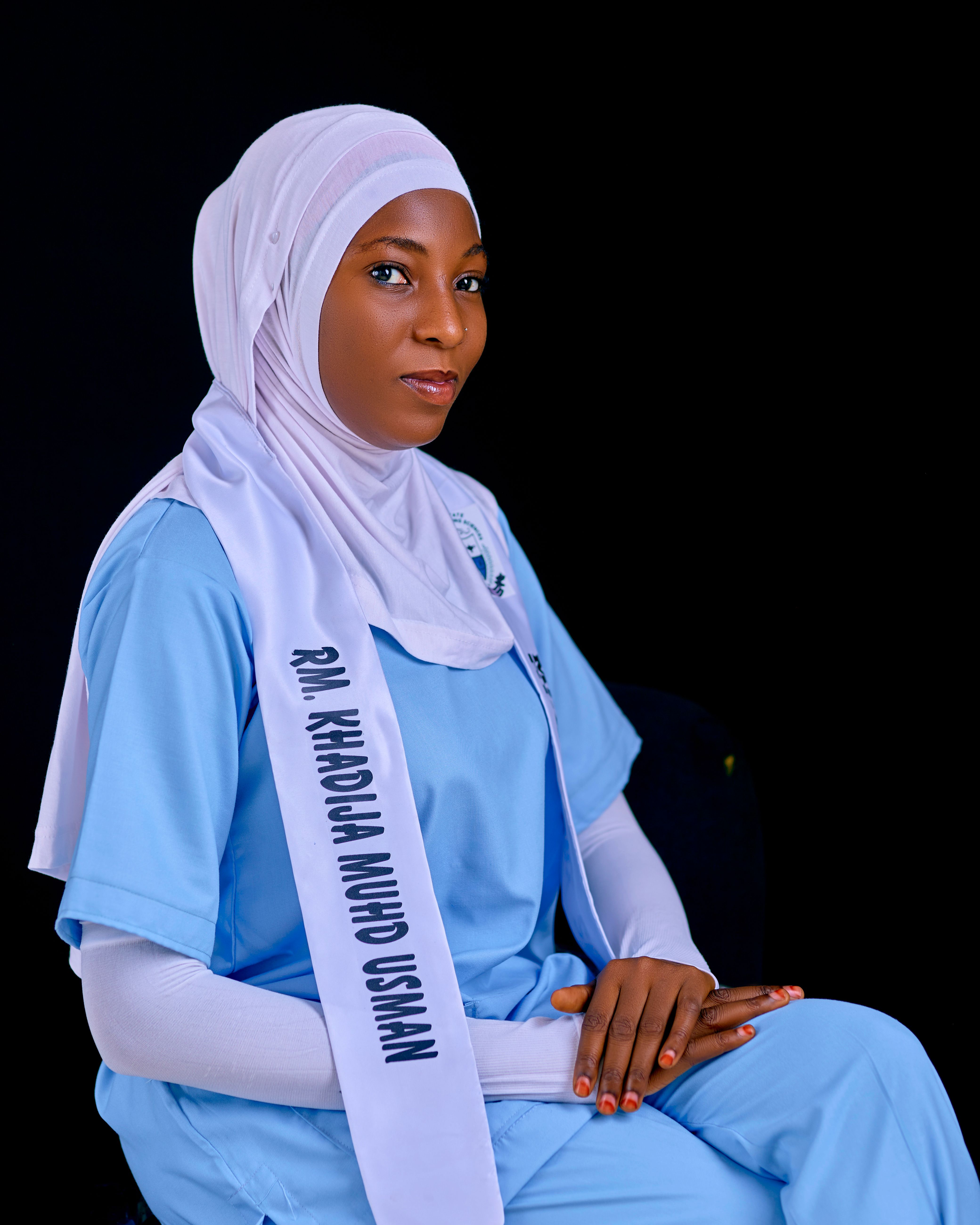 Portrait of a confident woman in medical attire and hijab against a dark background.