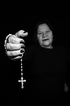 A black and white portrait of an elderly woman holding a rosary, symbolizing faith and devotion.