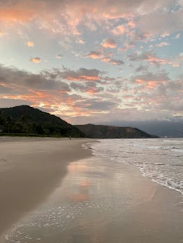 Serene beach scene at sunset with beautiful clouds and a mountain view.