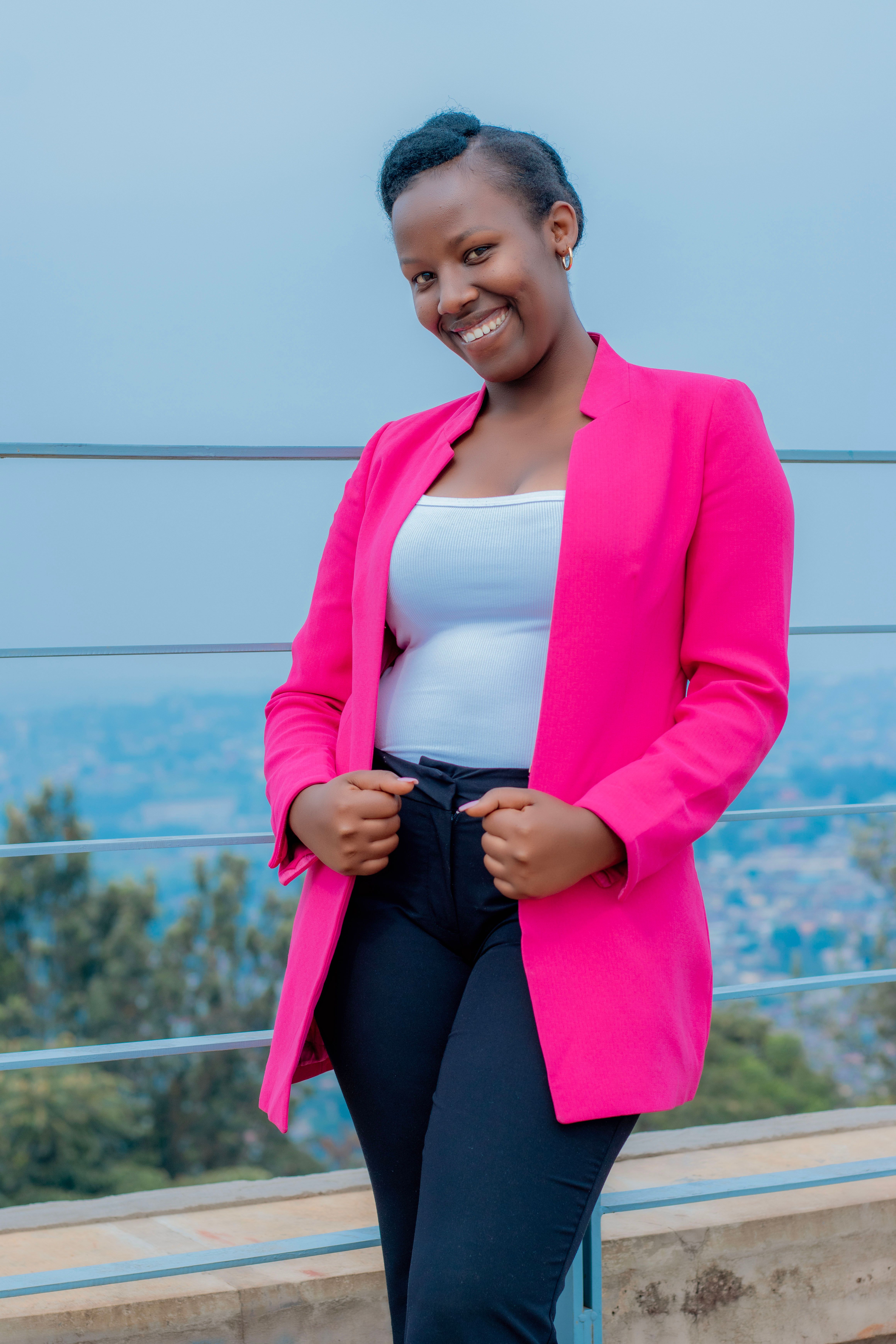 Confident young woman smiling brightly while standing outdoors in a vibrant pink blazer.