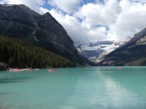 Scenic view of Lake Louise with mountains, canoes, and vibrant blue water.