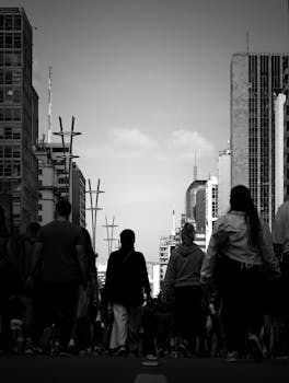 Black and white photo of people walking in a bustling city street lined with tall buildings.