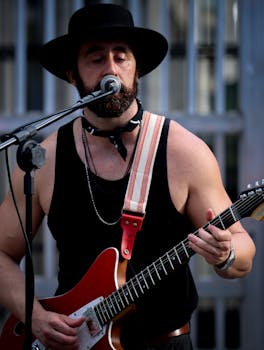 A bearded musician in a black hat playing electric guitar and singing outdoors.
