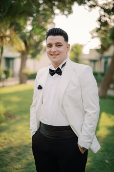 Dapper man in a white tuxedo smiling confidently at an elegant outdoor event.