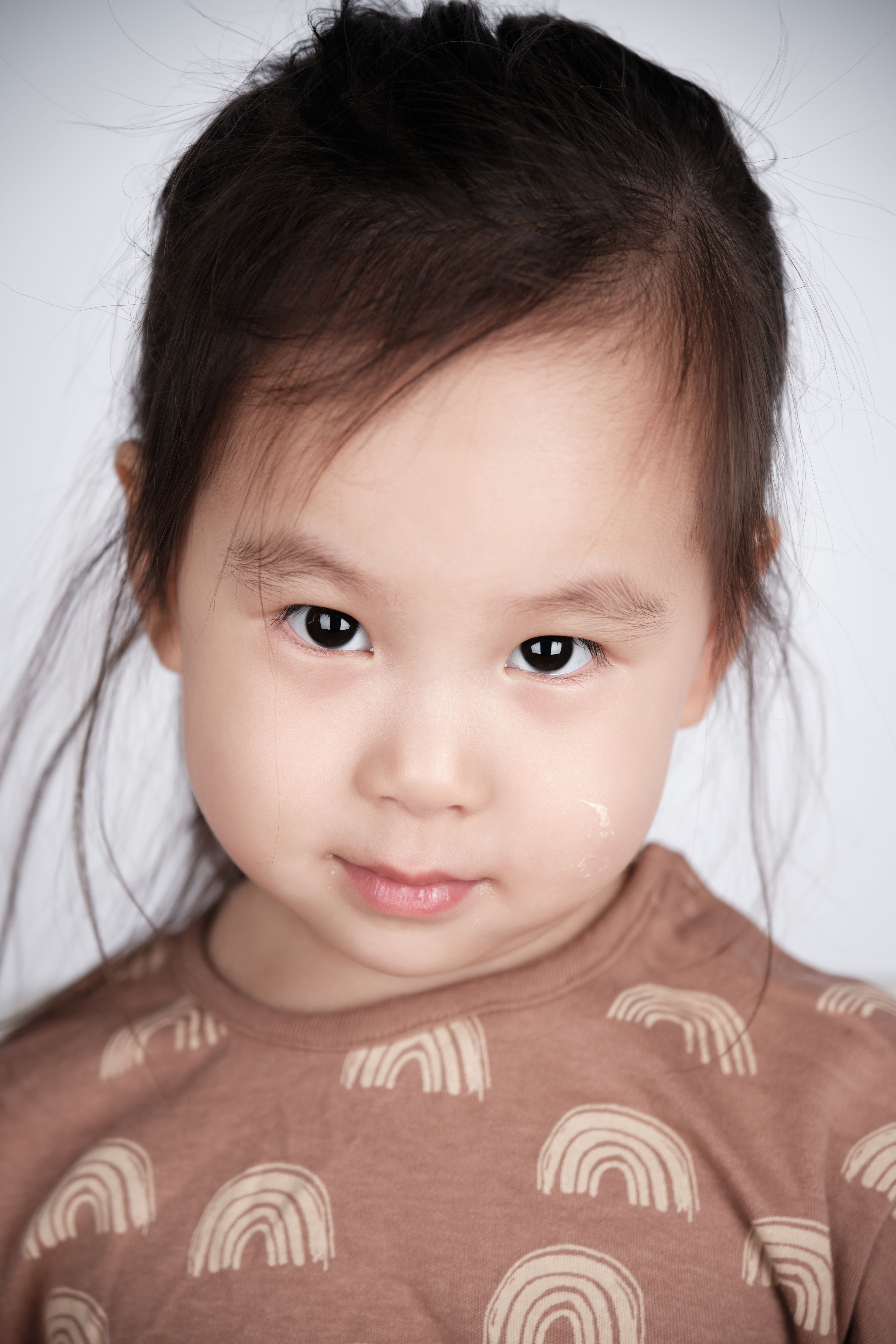 Close-up portrait of a young girl with a curious expression wearing a rainbow-patterned shirt.