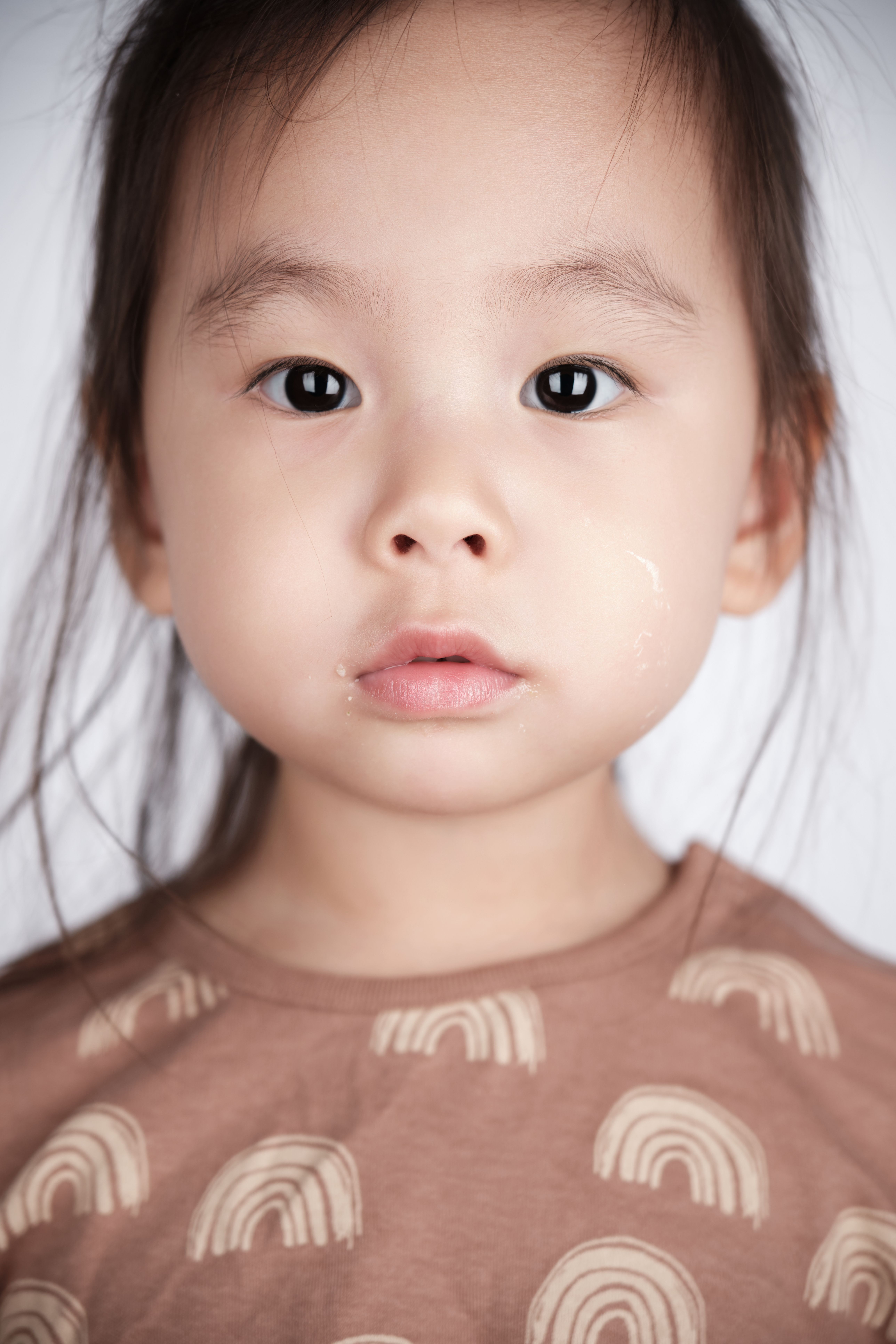 Close-up portrait of a young child wearing a rainbow-patterned shirt, looking directly at the camera.