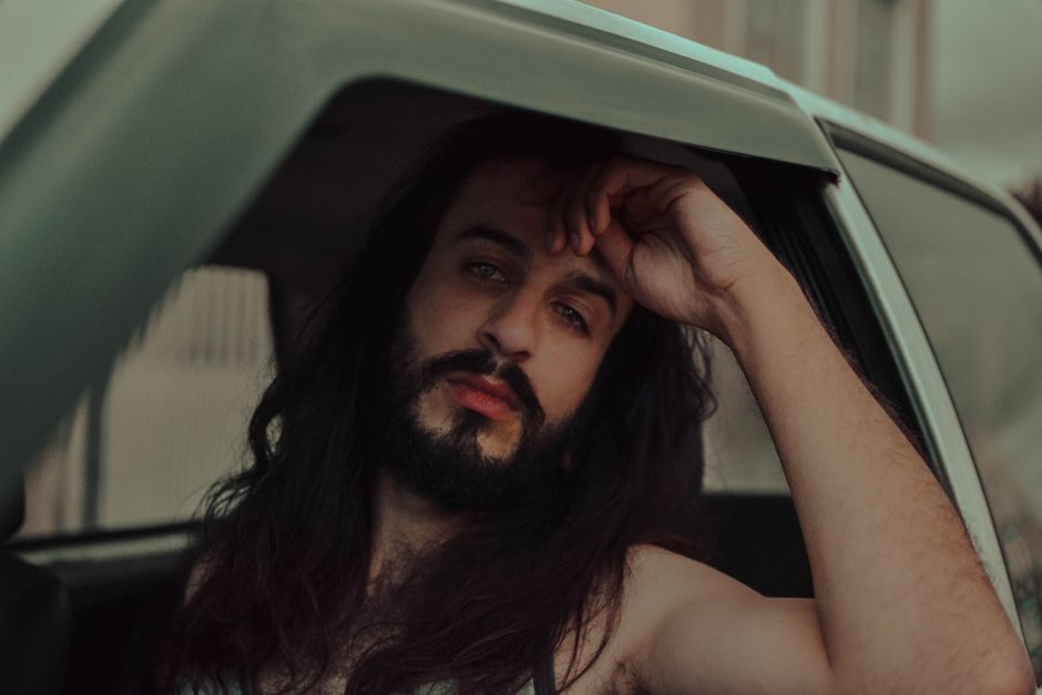 A man with long hair gazes pensively through a vehicle window, conveying introspection.