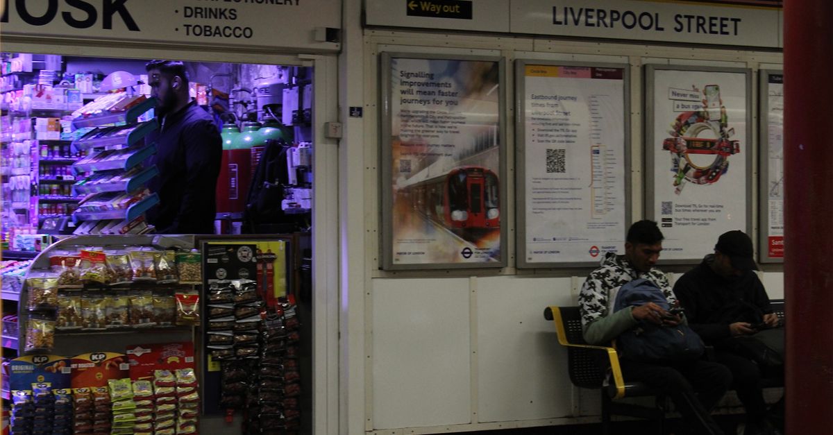 Night scene at Liverpool Street Station with a vibrant kiosk and waiting passengers.