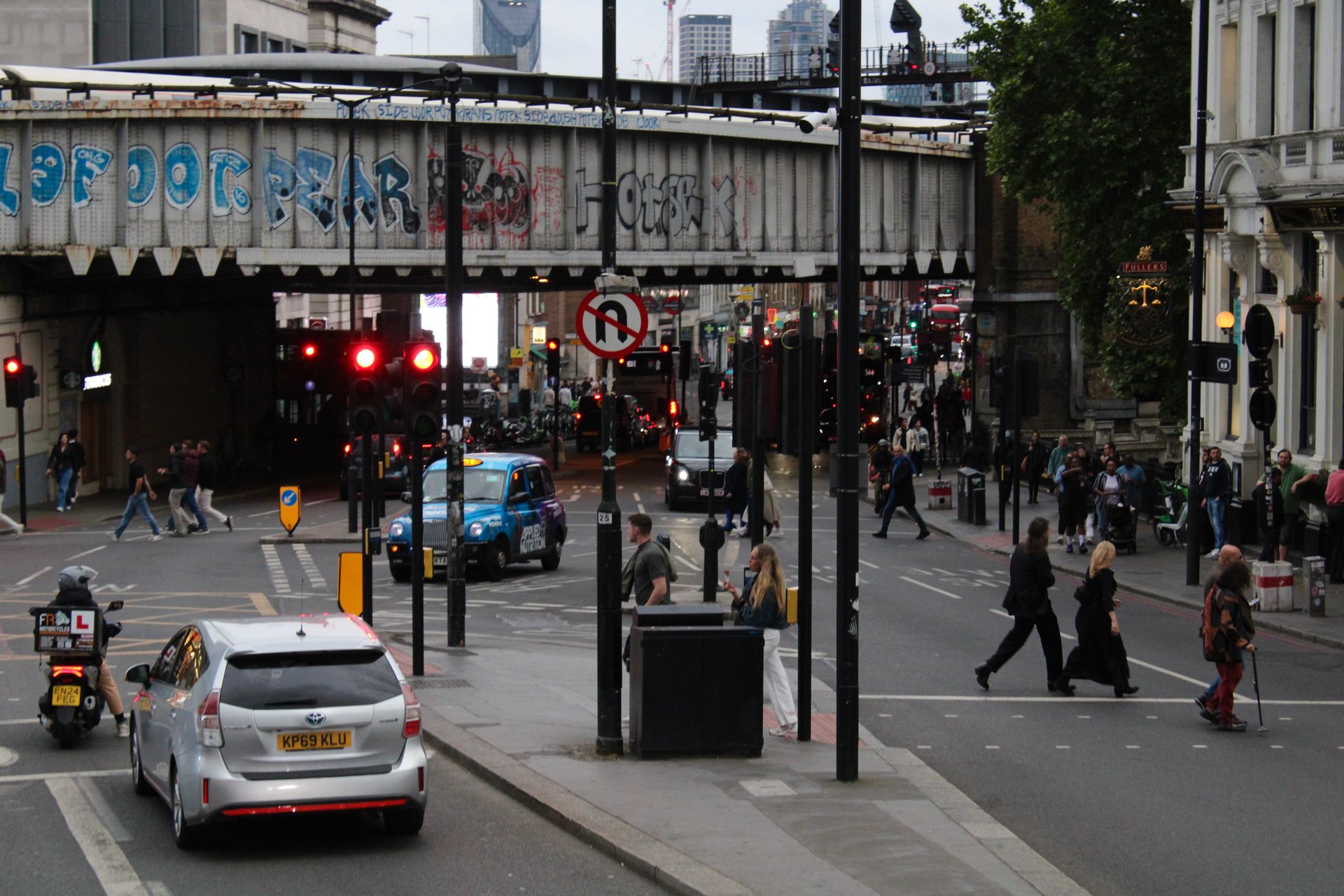 London street scene with traffic, pedestrians, and graffiti-covered bridge.