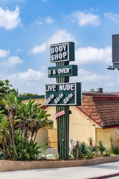 Strip club sign in West Hollywood, California, showcasing 'Body Shop' with palm trees in the background.