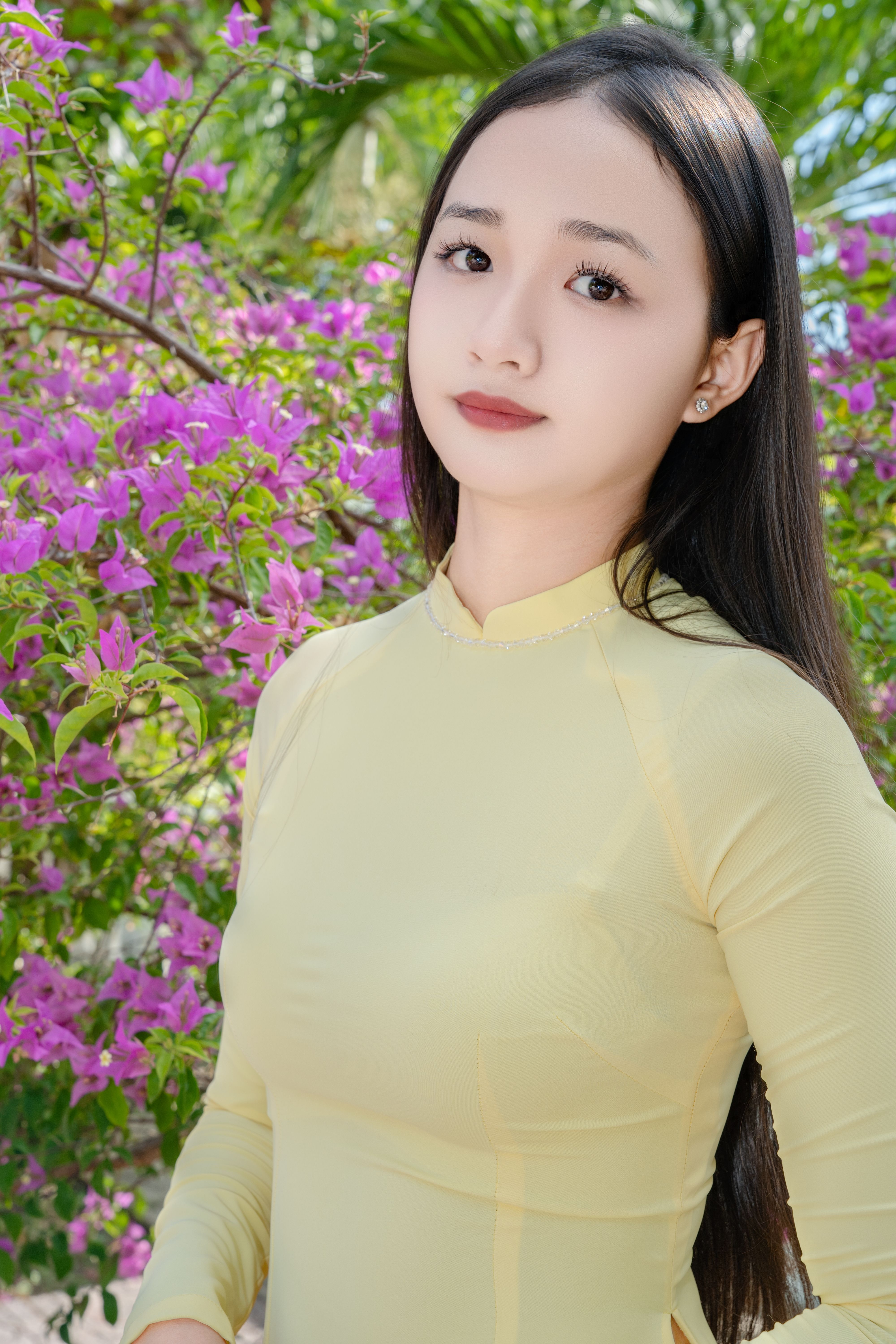 Portrait of a young woman in a yellow dress surrounded by vibrant bougainvillea flowers.