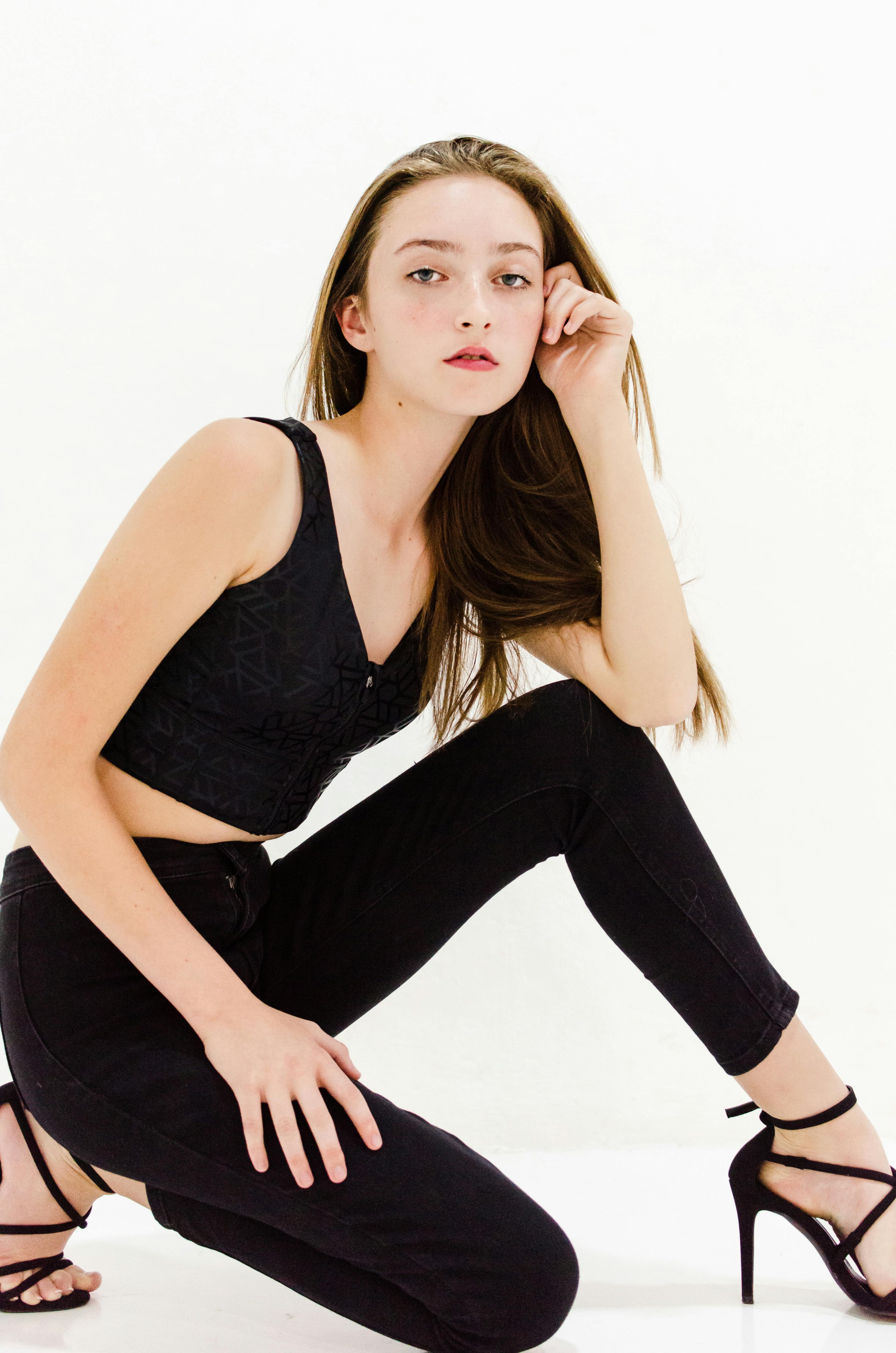 Elegantly posed young woman in black outfit on white backdrop, showcasing modern fashion.