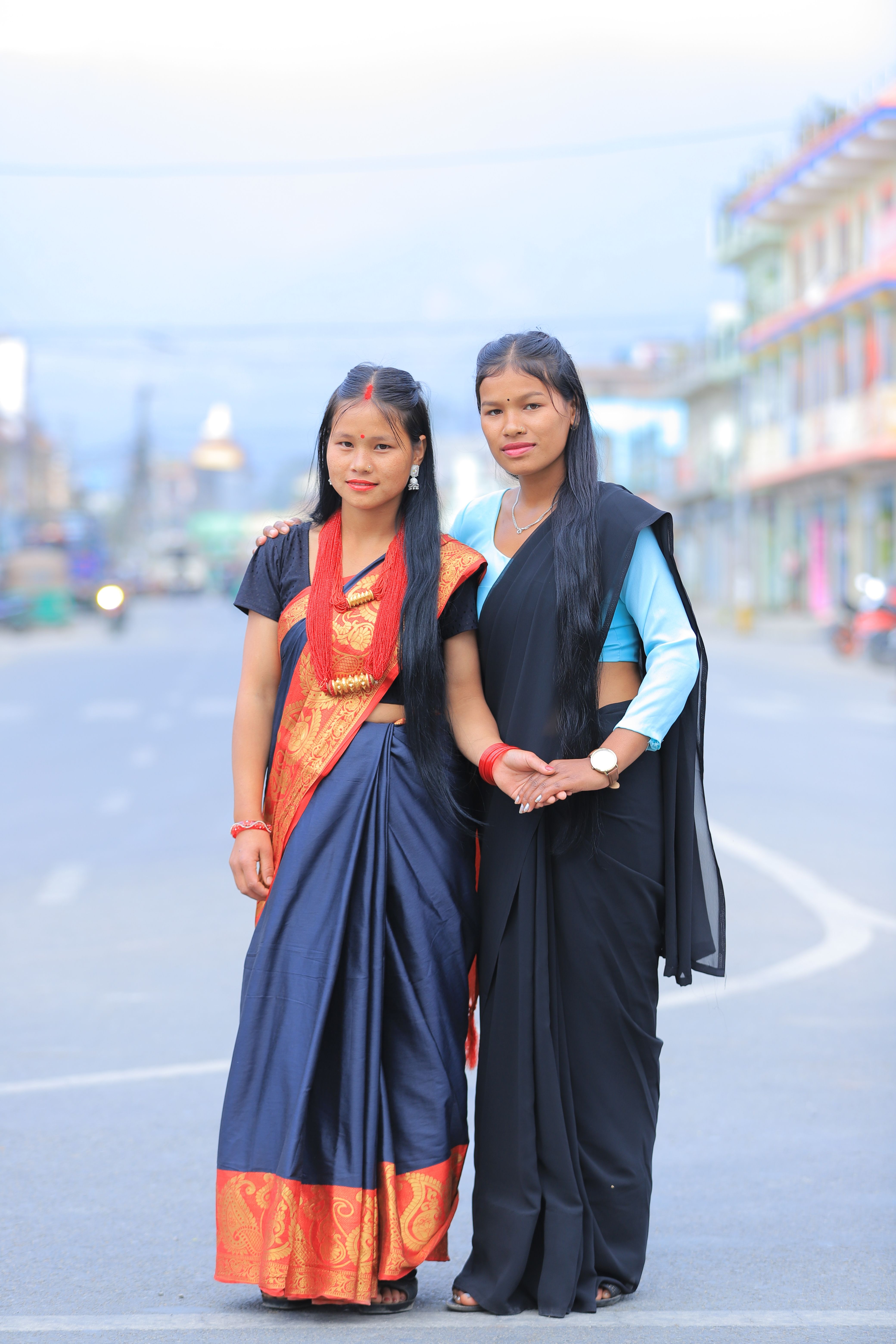 Two women in traditional attire standing outdoors on an empty street.