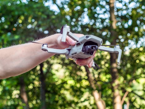 A hand holds a drone ready for flight in a lush forest environment, showcasing modern technology.